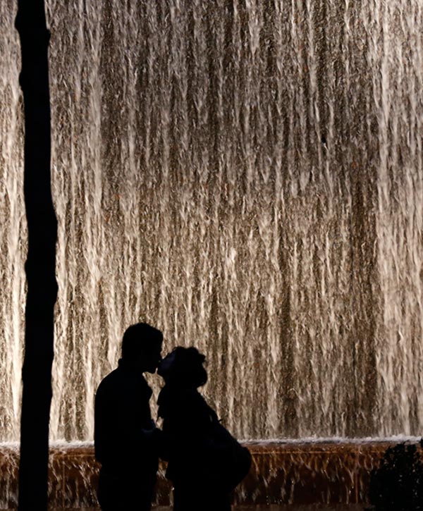 A couple is silhouetted as they kiss in front of a wall waterfall in a small park in New York City. New York was the 11th most expensive place to take someone out on a date.
