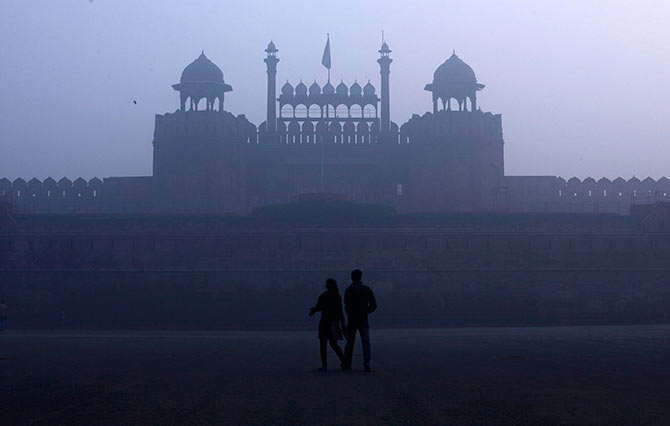 A couple walks in front of the historic Red Fort amid dense fog on a cold winter morning in the old quarters of Delhi.