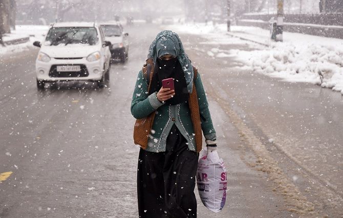 A girl using mobile phone walks on a road during fresh snowfall in Srinagar. Photograph: ANI Photo