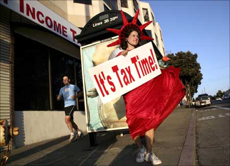 Denise Jameson wears a costume while carrying a sign to remind people passing on foot and in cars that it is income tax filing season outside a tax consulting business in San Francisco, California.