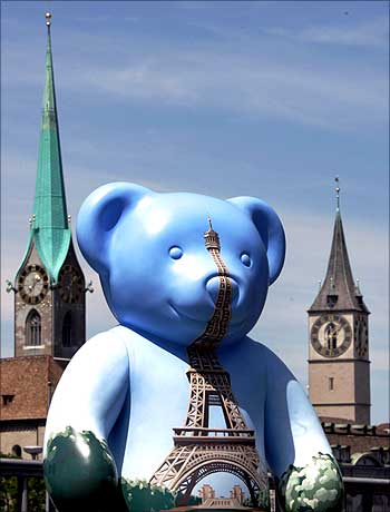 A teddy bear with a painted Eiffel tower on its chest stands in front of the Fraumuenster church (L) and the St. Peter church on the Quai bridge in Zurich.
