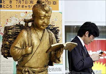 A man reads a book next to a statue in front of a book store in Tokyo.