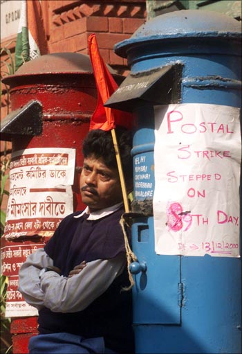 A postal employee leans against a letter box in Kolkata.
