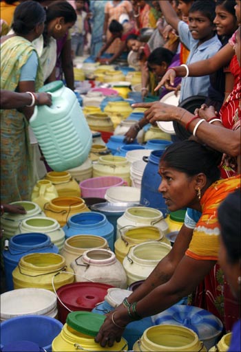 Residents of a slum stand with empty water containers at a roadside in Kolkata.