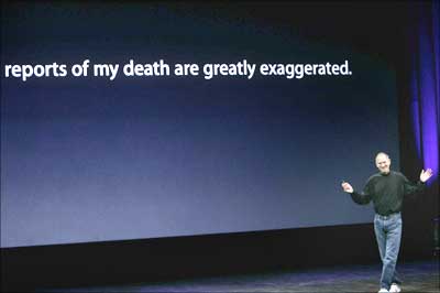 Steve Jobs takes the stage beneath a sign that makes light of reports on his health.