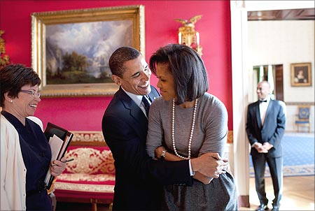 Obama hugs his wife, Michelle, in the White House Red Room as Senior Advisor Valerie Jarrett smiles.