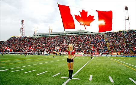 A Calgary Stampeders cheerleader flies a Canadian flag during Canada Day.