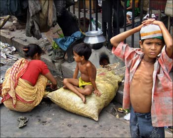 A homeless Indian boy waits for food beside a pavement as his mother cooks rice in Kolkata.