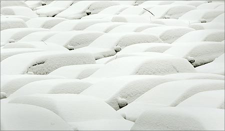 Snow covered cars are parked at a car park.