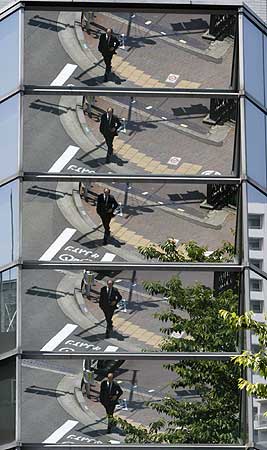 A businessman is reflected on an office building in Tokyo.