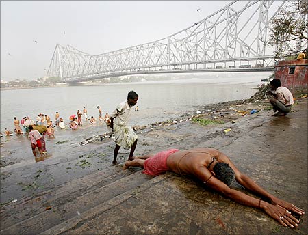A Hindu devotee prays on the bank of the Ganges river against the backdrop of Howrah Bridge.
