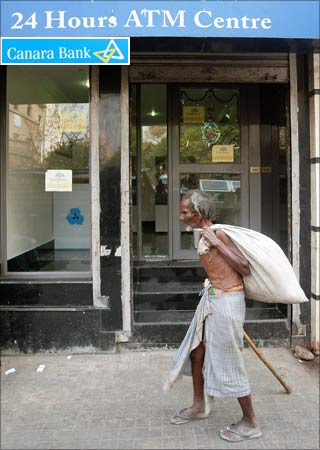 A man walks past a bank's ATM kiosk in Kolkata. (Inset: Canara Bank logo).