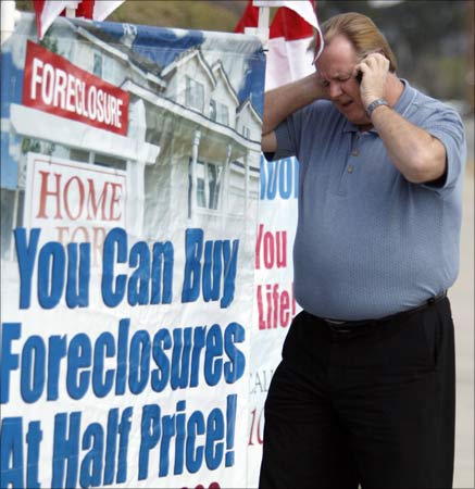 Home Center Realty owner Ron Barnard talks on his cell phone as he stands next to a sign advertising