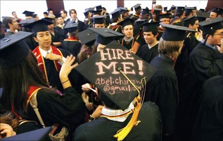 A graduating student displays a 'Hire me' sign written on his mortar board.