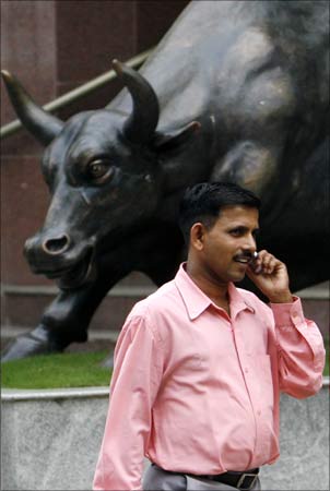 A man speaks on a phone in front of a bronze replica of a bull at the gates of Bombay Stock Exchange.