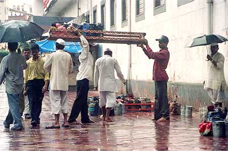 A dabbawallah helps his colleague lift a crate full of tiffin boxes