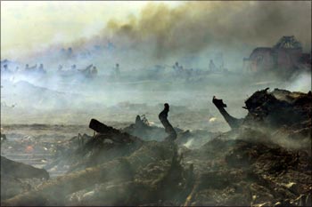 Indian tsunami survivors look for their belongings amid the debris of their tsunami-destroyed houses that are being burnt by Indian workers in Nagapattinam.