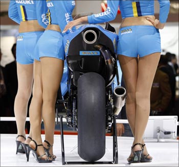 Models at the Suzuki Motor Corp booth pose with a Rizla Suzuki MotoGP racing motorcycle at the 41st Tokyo Motor Show.
