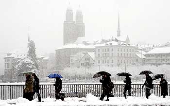 People cross the Quaibruecke bridge in front of the Grossmuenster church during snowfall in Zurich.