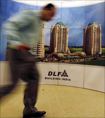 A man walks past a banner of Indian property developer DLF Ltd.