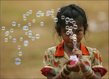 A girl selling bubble-making toys, blows bubbles to attract buyers in Mumbai.