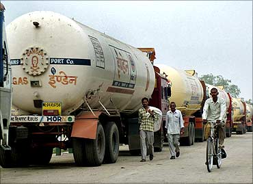 People pass trucks parked near an oil refinery.