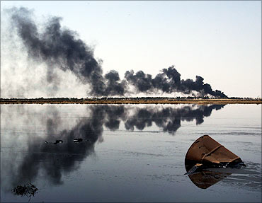 An oil lake lies near a blazing pipeline outside Basra.