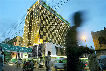 Pakistani pedestrians walk past an illuminated building on the eve of independence day in Karachi.