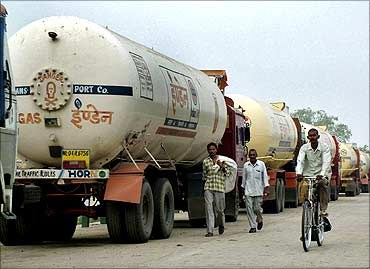 People pass trucks parked near an oil refinery