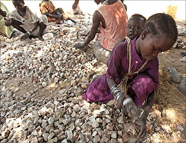 A girl carries her sister as she breaks rocks into smaller pieces to be sold for construction purposes in Juba.