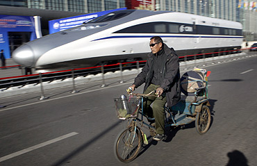 A resident rides a tricycle past the head of a CRH (China Railway High-speed) Harmony bullet train.