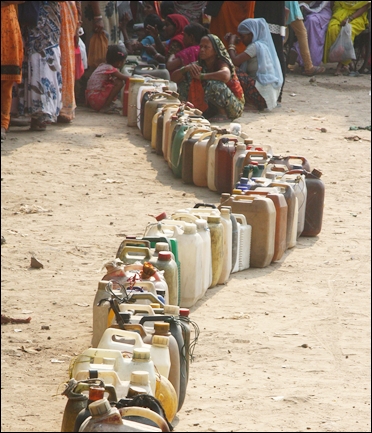 People wait with cans to collect kerosene from the ration shop.