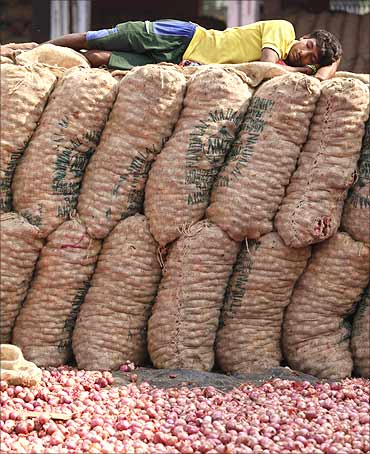 A labourer takes a nap on sacks of onions at a wholesale vegetable market.