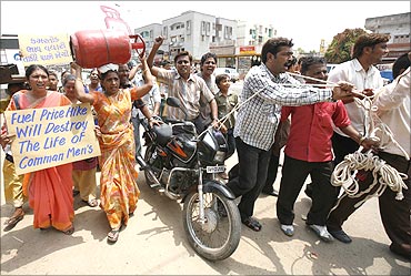 A woman carries a cooking gas cylinder as men pull a string tied to a motorbike during a protest.