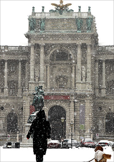 A woman with a dog walks over Heldenplatz square in front of the historic Hofburg palace.