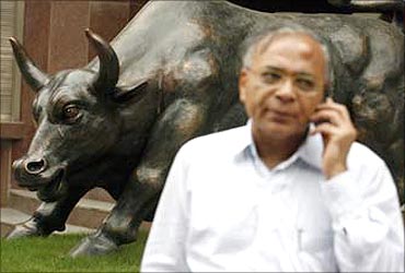 An investor speaks on a mobile phone in front of a bronze replica of a bull at the gates of Bombay Stock Exchange building in Mumbai.