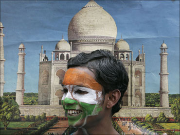 A schoolboy with his face painted in the colours of the Indian national flag stands in front of a photograph of the Taj Mahal.
