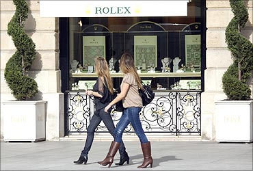 Women walk past a window display of luxury goods maker Rolex in Paris' Place Vendome.
