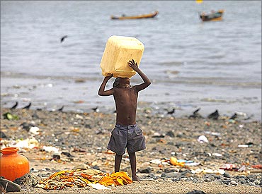A homeless child tries to drink water from a plastic container on a beach in Mumbai.