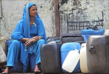 A woman sits on empty water buckets to be filled with drinking water.