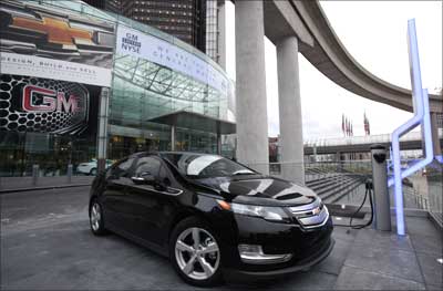 A Chevrolet Volt electric vehicle sits plugged into a charging station in front of GM's headquarter.