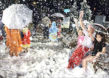 Tourists pose for photographs as soap suds simulating snow fall outside a mall in Singapore.