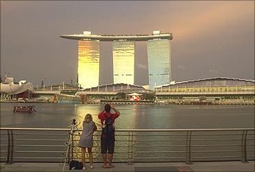 Tourists stand at a promenade across the water from the Marina Bay Sands.