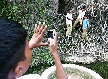 A schoolboy uses his cell phone to take a picture of classmates hanging onto cement roots.