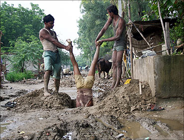 Labourers hold their co-worker to install underground electric cables at Noida.
