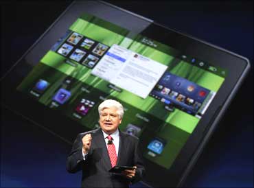 Mike Lazaridis, president and co-chief executive officer of IM, holds the new Blackberry PlayBook with a screen projection of the devic.