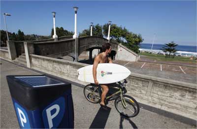 A surfer rides his bicycle next to a solar-powered parking meter at Bondi beach in Sydney.