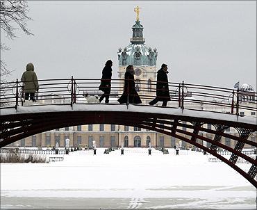People walk over a bridge in front of snow covered Charlottenburg castle in Berlin.