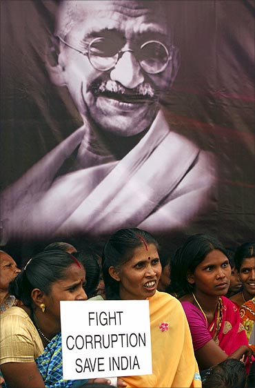 A supporter of Anna Hazare holds a placard in front of a portrait of Mahatma Gandhi.