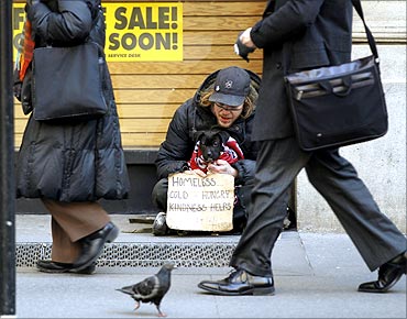 Pedestrians walk past a man as he panhandles for money sitting with a puppy in New York.